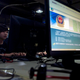 Computer users sit near a monitor display with a message from the Chinese police on the proper use of the Internet (Associated Press)